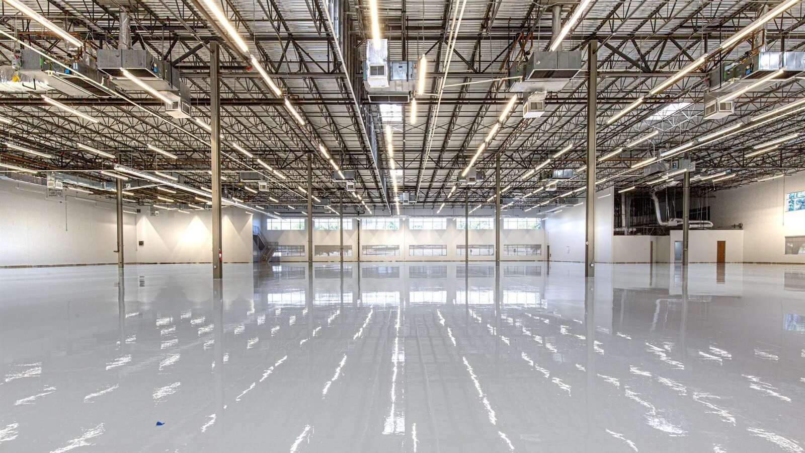 A large interior space with a glossy pale resin-coated floor reflecting overhead lights