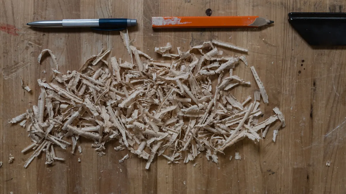Pile of wood shavings beside a pen on a wooden table