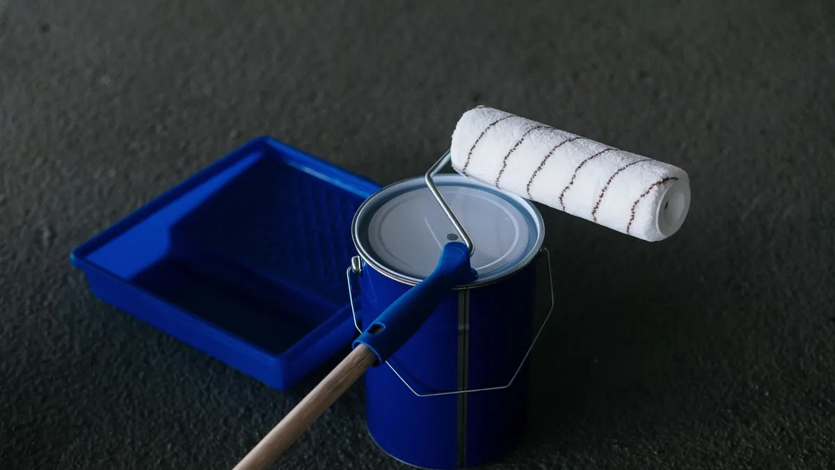 Paint can, roller and blue paint tray on a dark floor