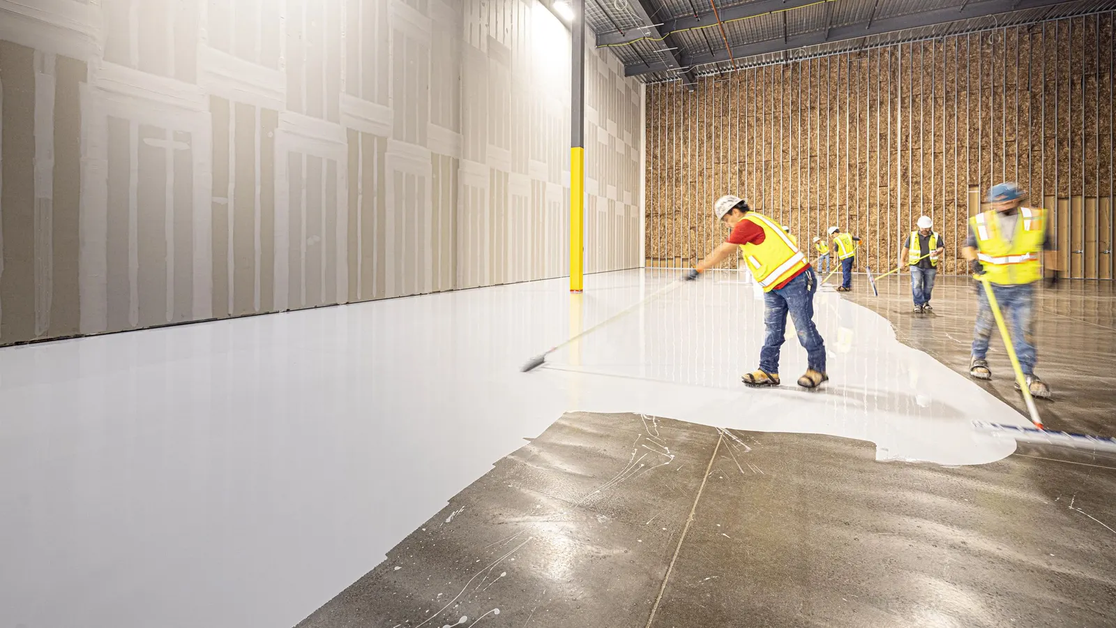 Workers in safety vests applying a floor coating in a large building