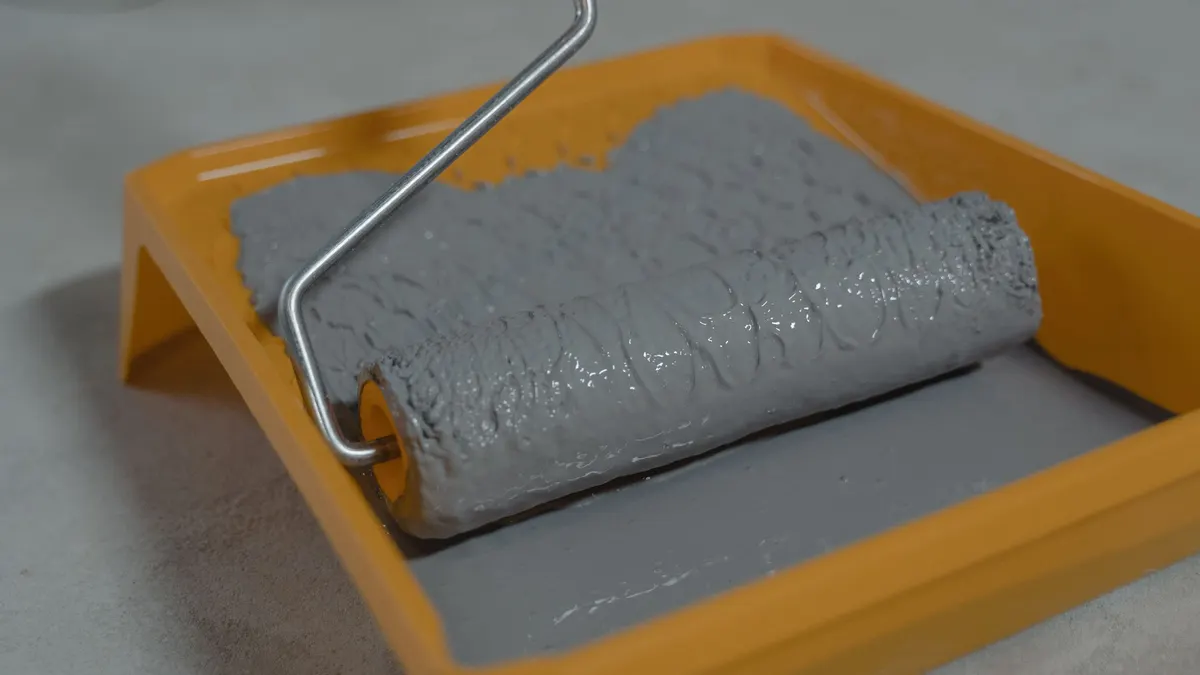 Gray floor coating on a roller in an orange paint tray