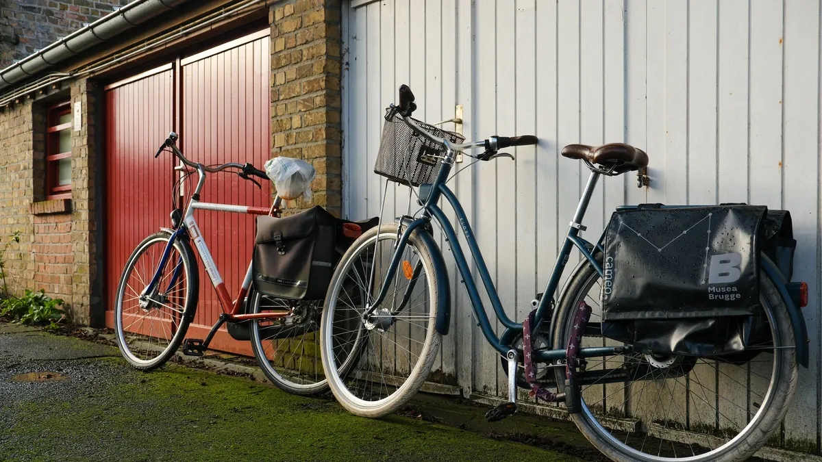 Two bicycles with baskets leaning against a wall