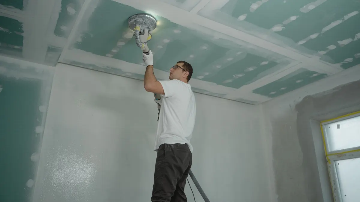 Worker sanding a newly drywalled ceiling