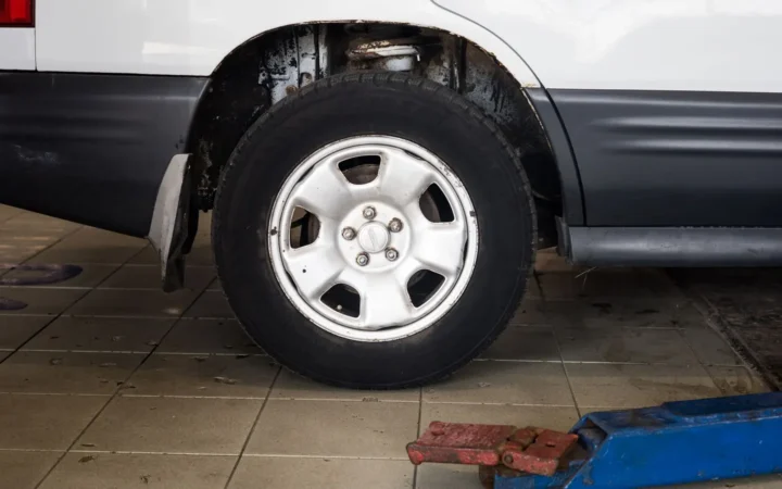 Car wheel on a tiled garage floor beside a blue floor jack