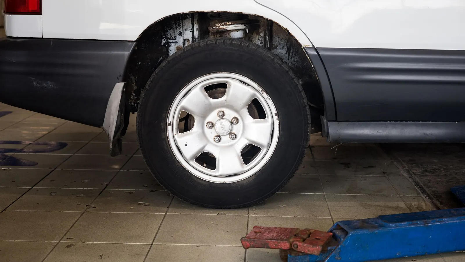 Car wheel on a tiled garage floor beside a blue floor jack