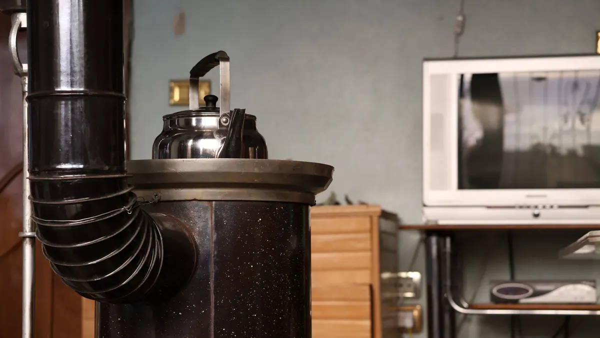 Black stove heater with a tall flue pipe and a kettle on top