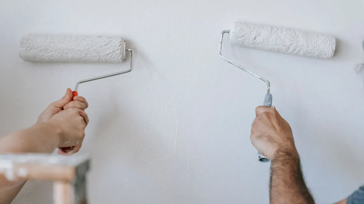 Two hands painting a white wall with paint rollers