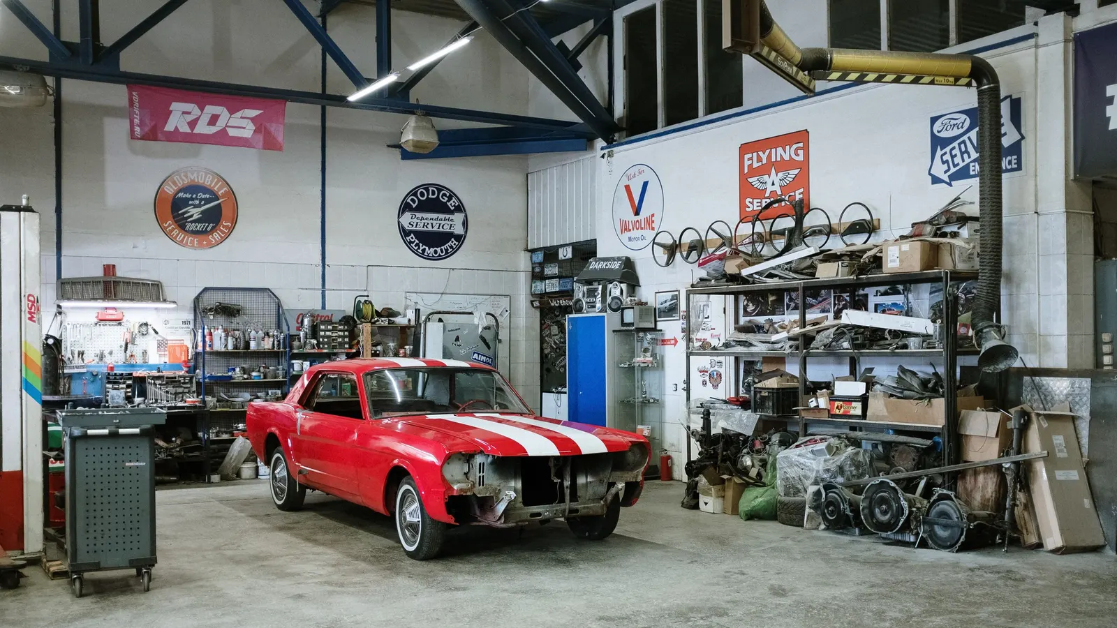 Garage with a red classic car, shelving and signs on the walls