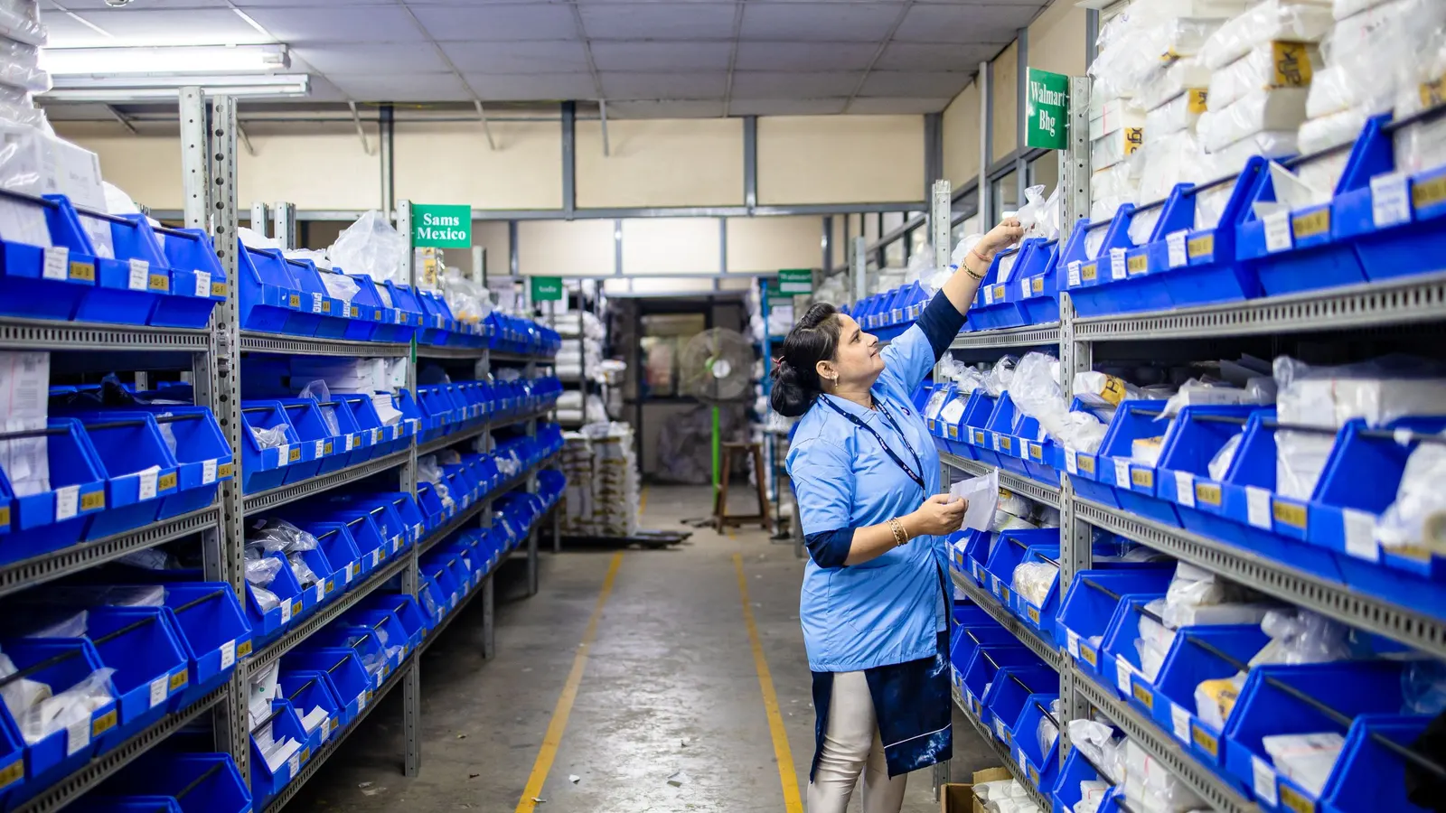 Person organizing blue bins on long metal shelving units