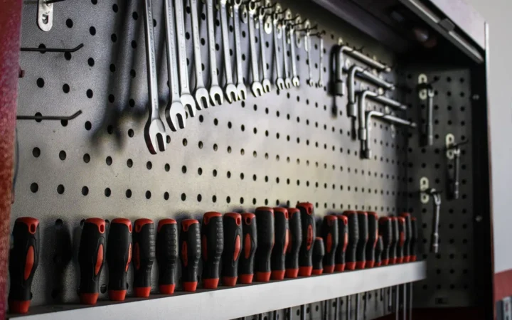 Black pegboard holding wrenches and screwdrivers above a shelf