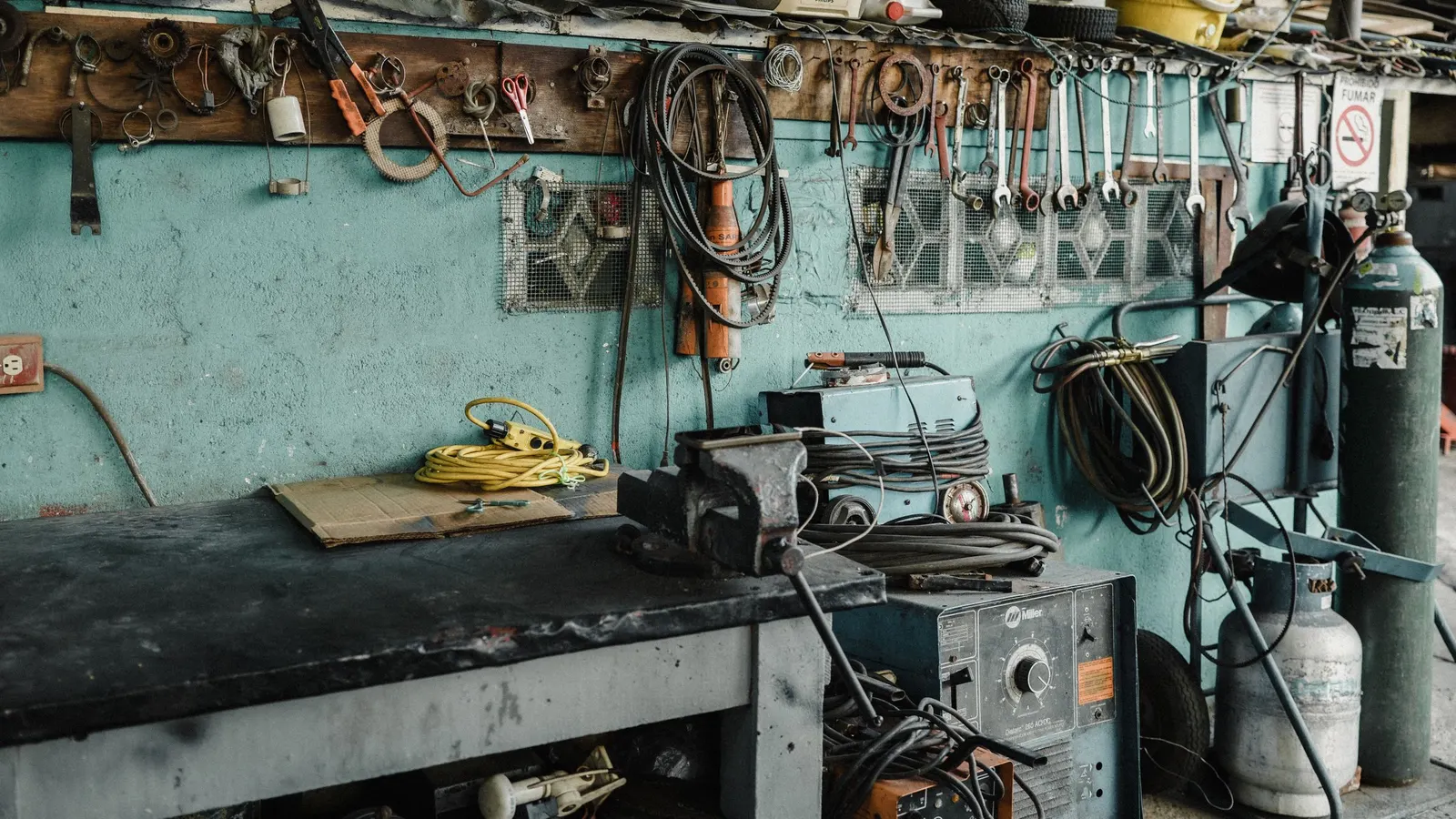 Workbench with a vise and tools against a teal workshop wall
