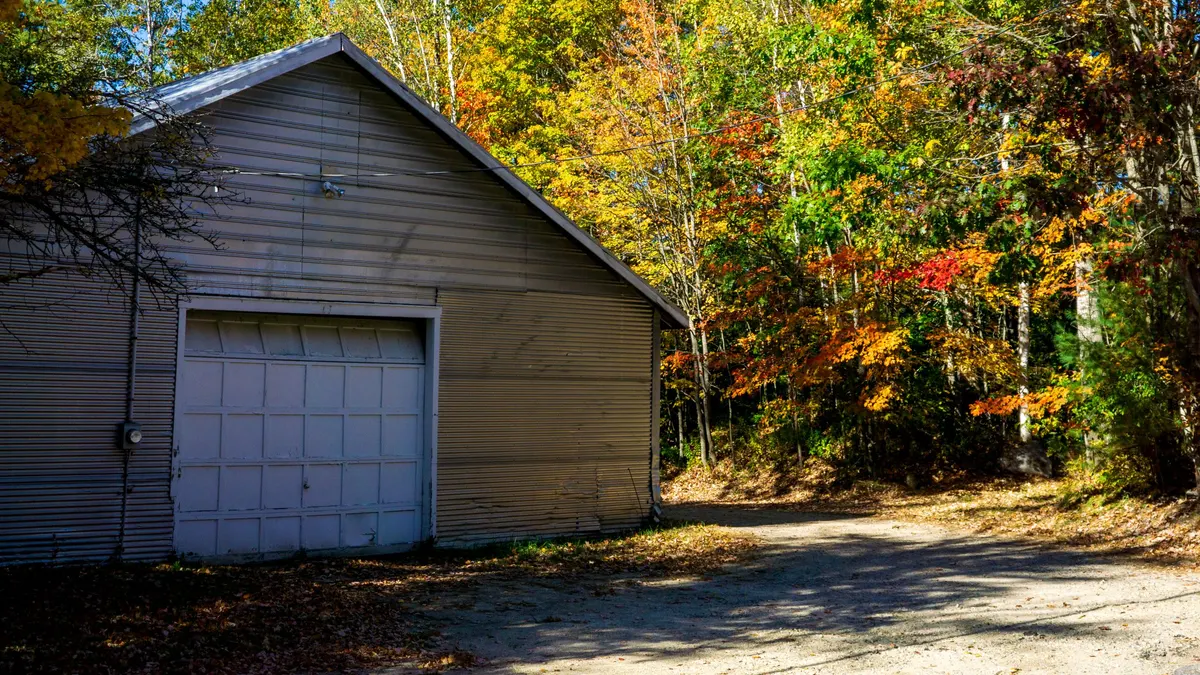 Detached garage among autumn trees with leaves on the ground
