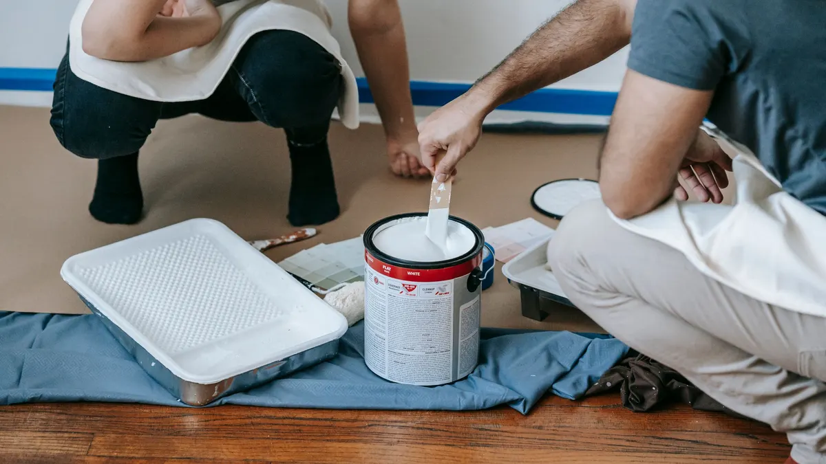 Two people mixing paint in a bucket on a drop cloth
