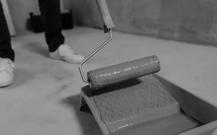 Person rolling gray coating from a tray onto a concrete floor