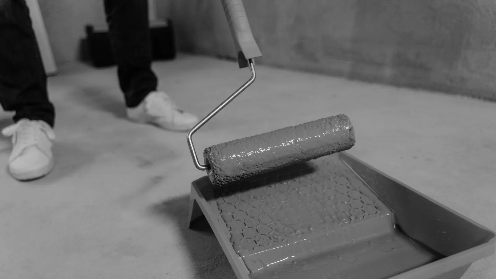 Person rolling gray coating from a tray onto a concrete floor
