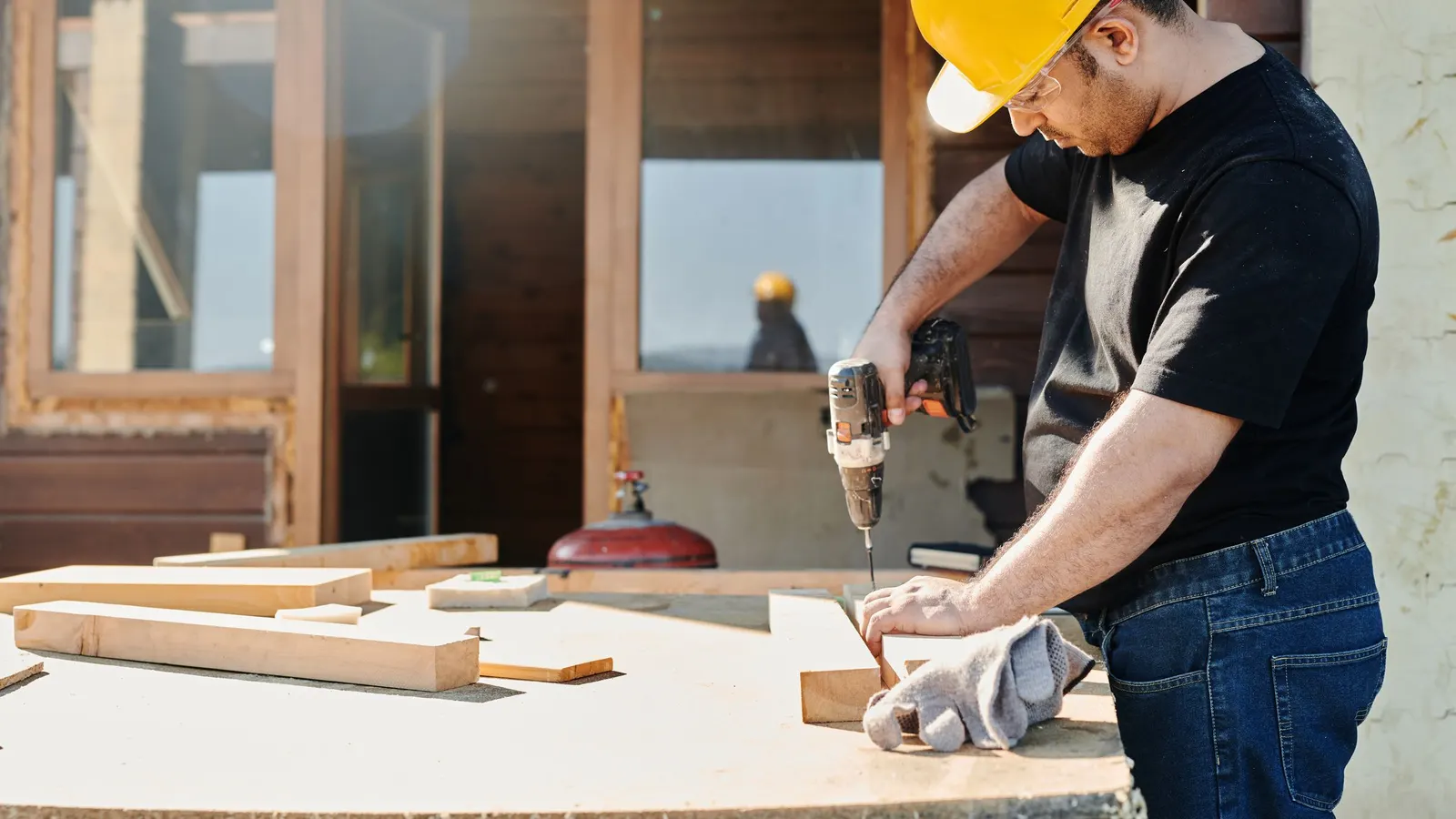 Man in a hard hat drilling into wood boards on a work table