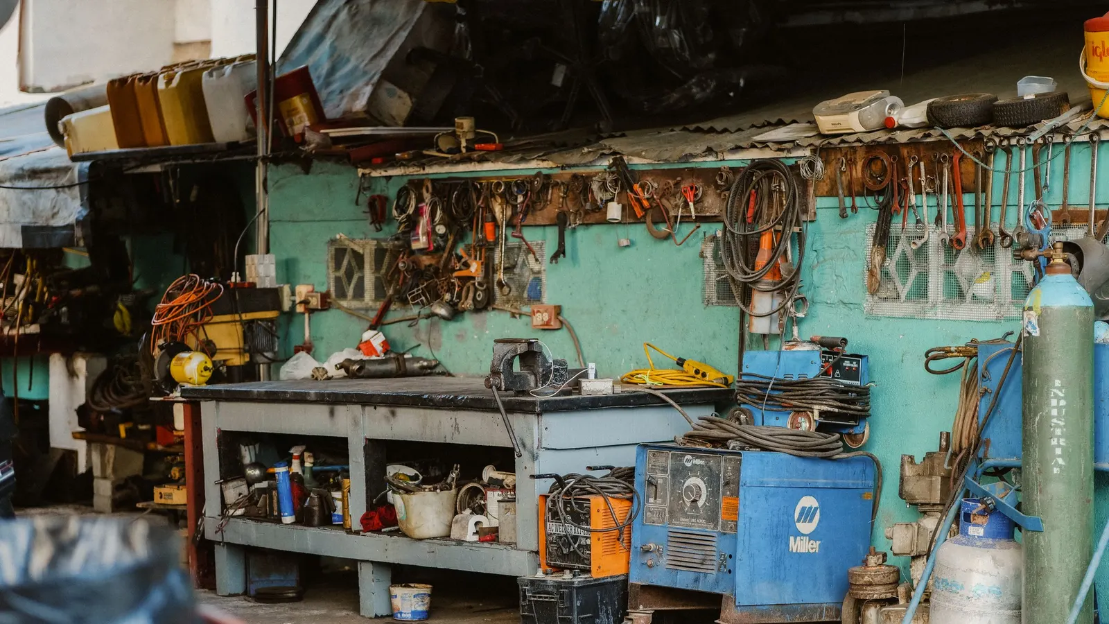 Busy garage workshop with a long workbench, tools on the wall and a welder