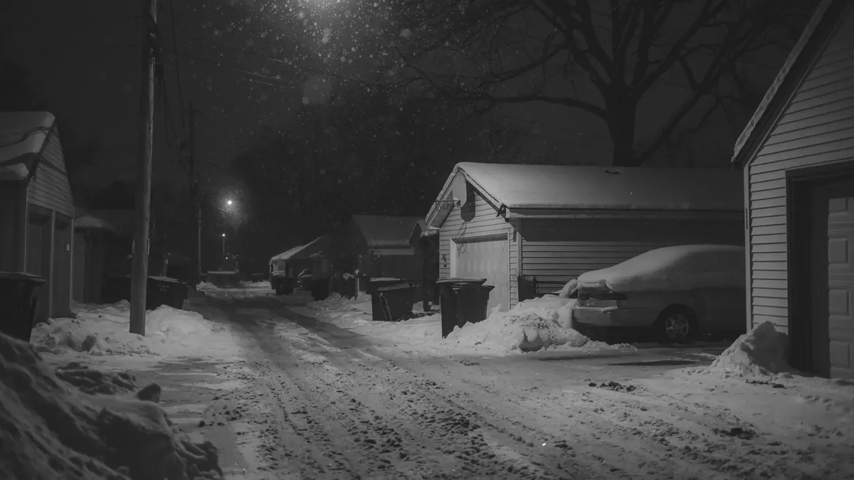 Snowy street at night with a car parked beside a garage