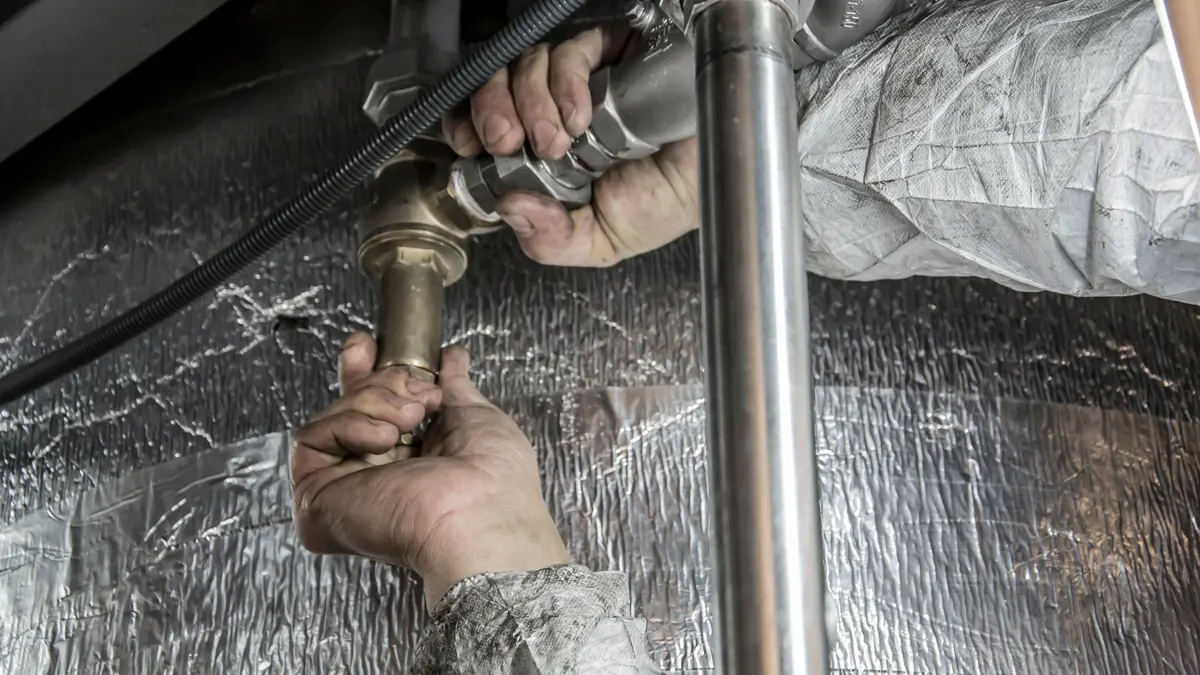 Hands working near reflective foil insulation around a pipe